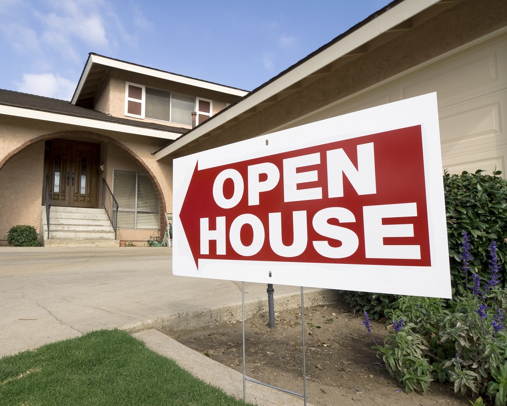 A home for sale shows the open house sign on a sunny afternoon.